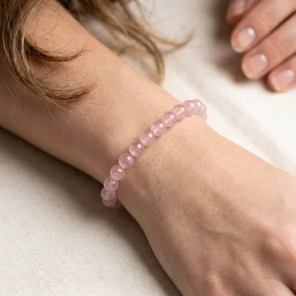 Rose Quartz Energy Bracelet worn on woman's wrist, delicate pink gemstone beads on soft background.